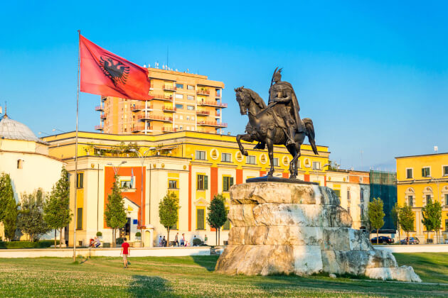 Skanderbeg-Denkmal auf dem zentralen Skanderbeg-Platz in Tirana, Albanien, mit albanischer Flagge im Vordergrund. | Gebeco